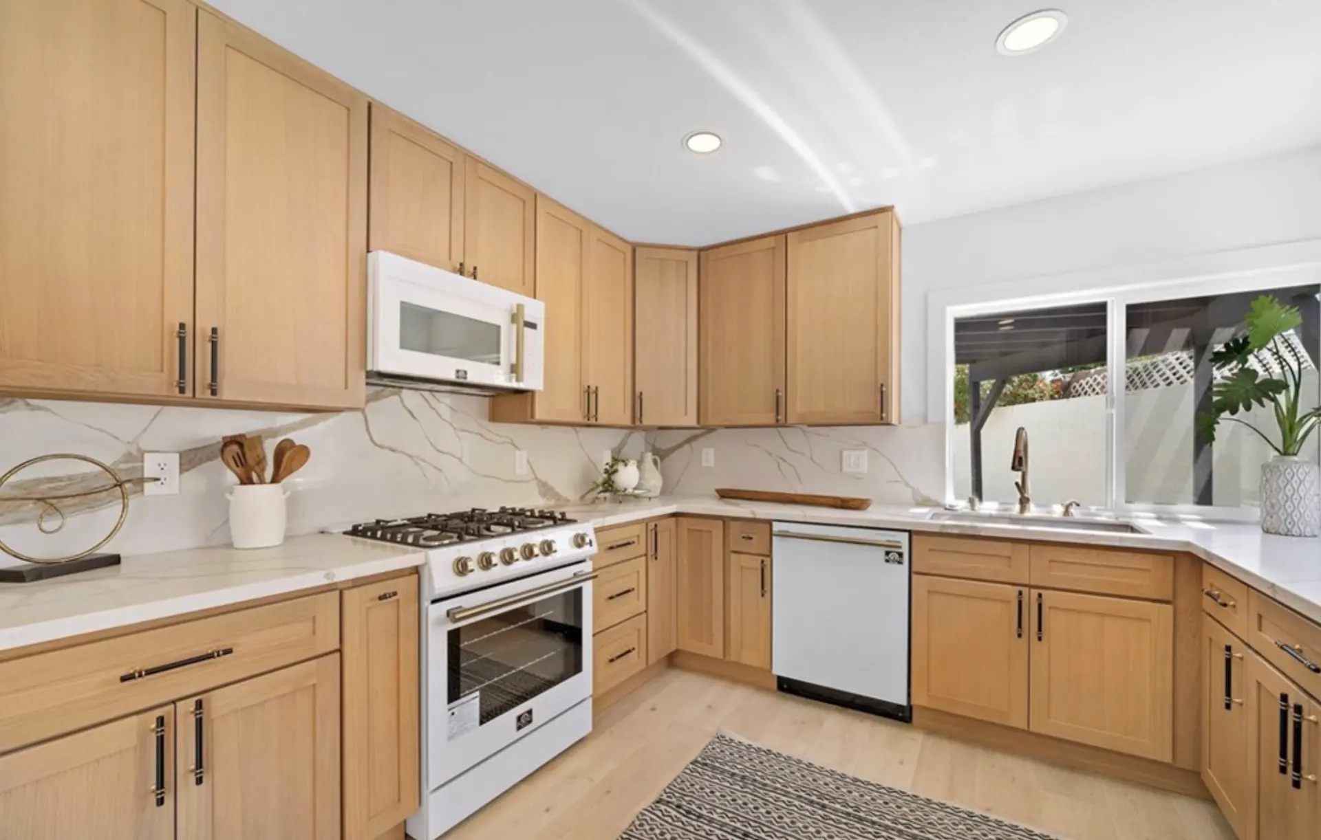 Remodeled kitchen with light oak soft-close cabinetry, quartz counters, marble-look backsplash and professional Forno range